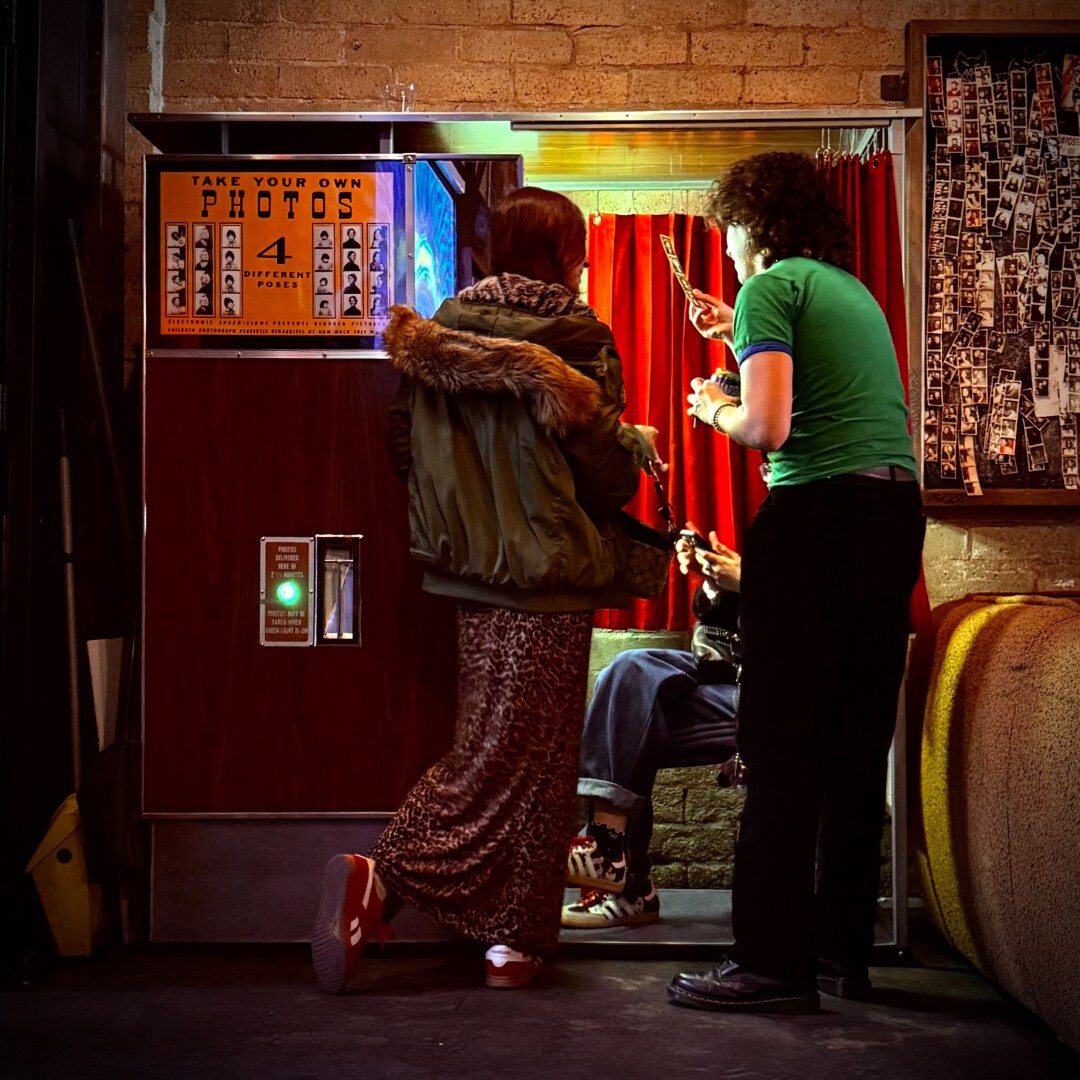 Three friends by a photobooth looking at their photos that have just printed.