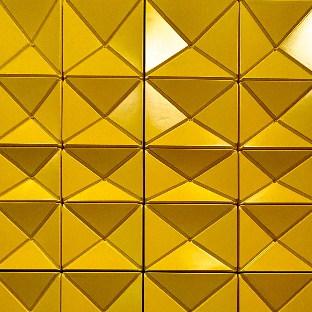 Close up of a yellow tile wall with triangles formed into the shape of rectangles and squares.
