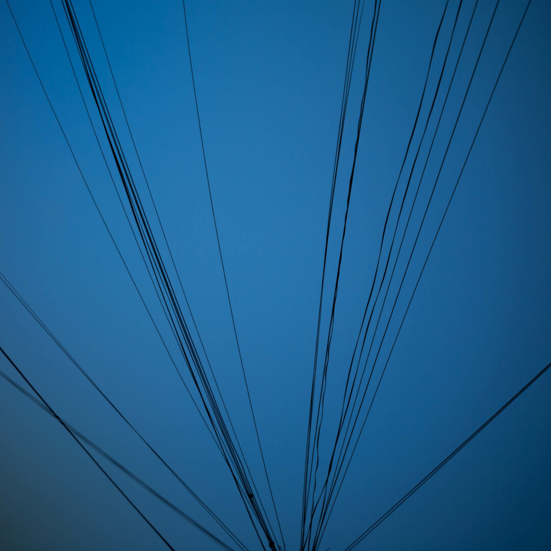 Photo of a faded blue sky with many thin black telephone lines radiating across it from just below the bottom of the from.