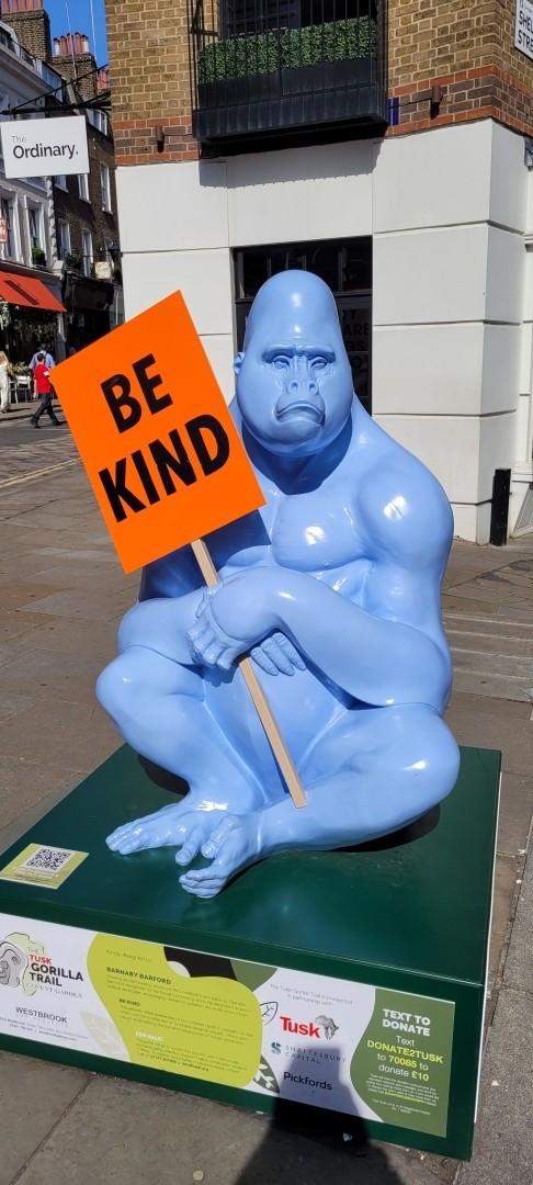 Sad gorilla sculpture statue holding a sign that says BE KIND