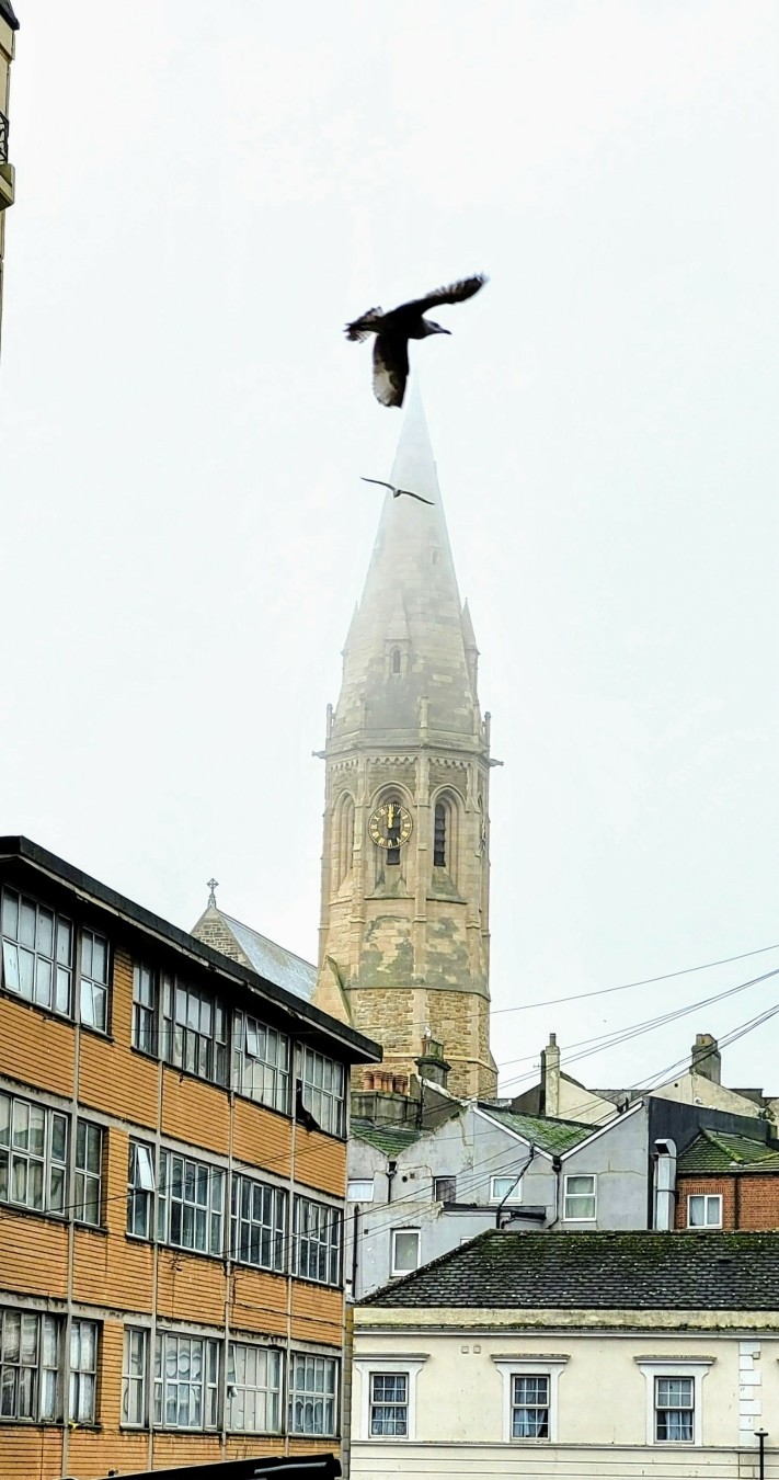 A cathedral spire gradually lost in mist above Battle town - gulls circle