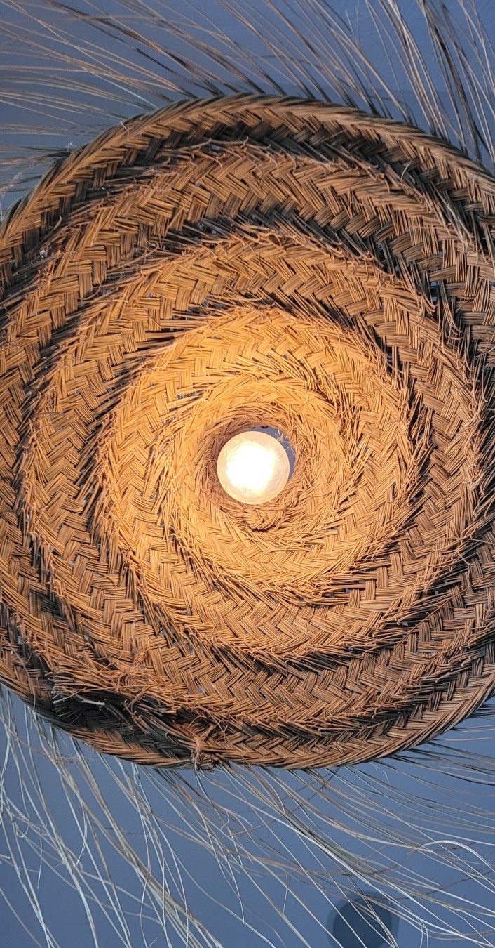 Up photo of a bright bulb in a spun wicker shade with whiskers. Looks like a sun halo.