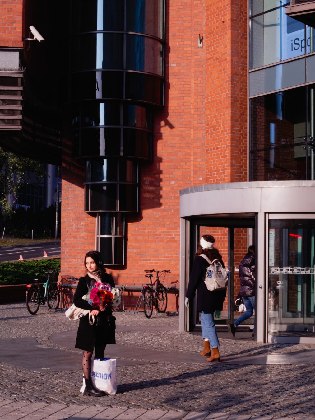 woman standing in front of a building with a revolving door, holding flowers