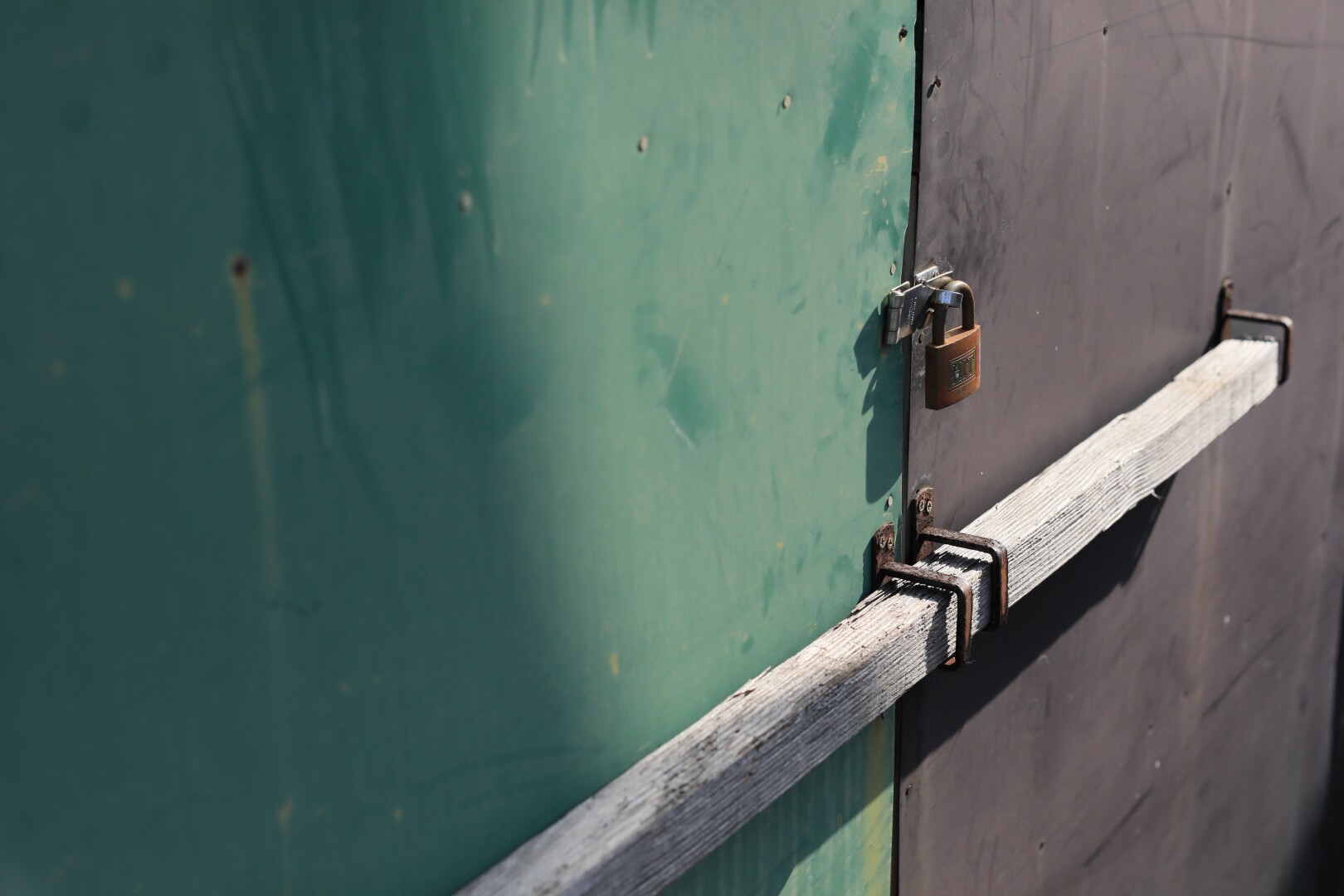 The light green and brown tin door is padlocked and barred.