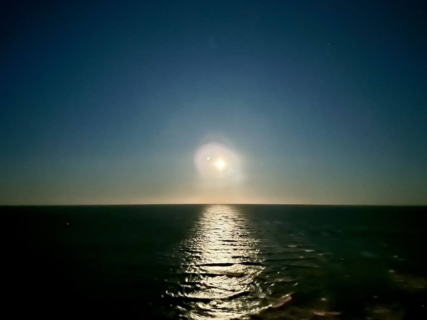 A photo taken from my hotel balcony in the middle of the night in December in Clearwater, FL. 

The image is split horizontally with the dark, calm water of the Gulf of Mexico below and the gradient shift of early morning skies. Blues and greens and yellows. The moon is visible just off of the horizon and it casts a reflection in the water down the center of the picture.