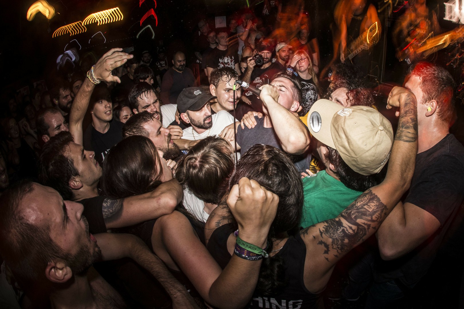 A photo of new york hardcore punkband Incendiary on stage in Paris.
On the photo the singer is in the middle of the crowd in front of the stage screaming in his microphone while leaning backward.
The crowd is on every side packed up against him screaming along.