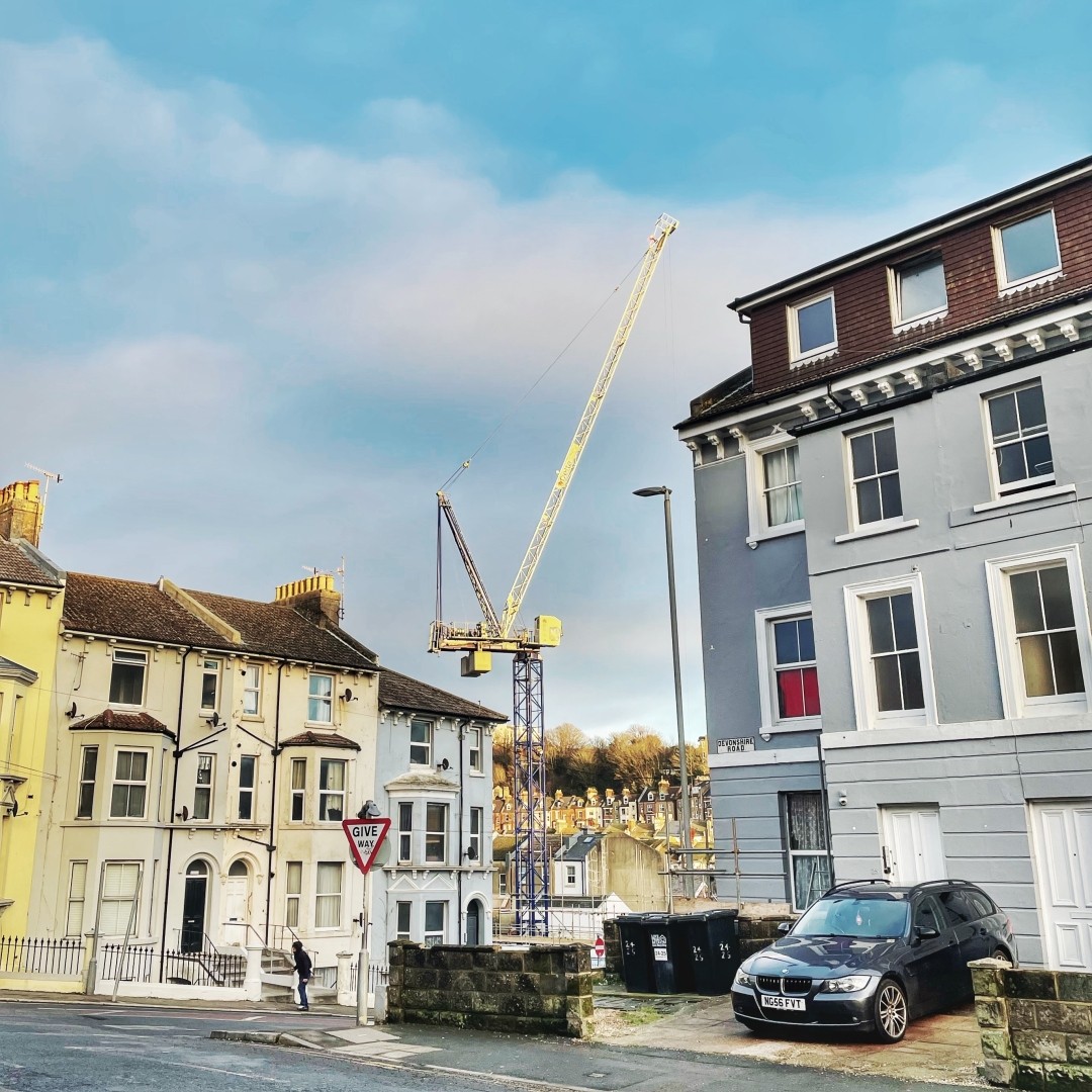 View of a tower crane on a building site visible against the sky between the ends of two Victorian terraces