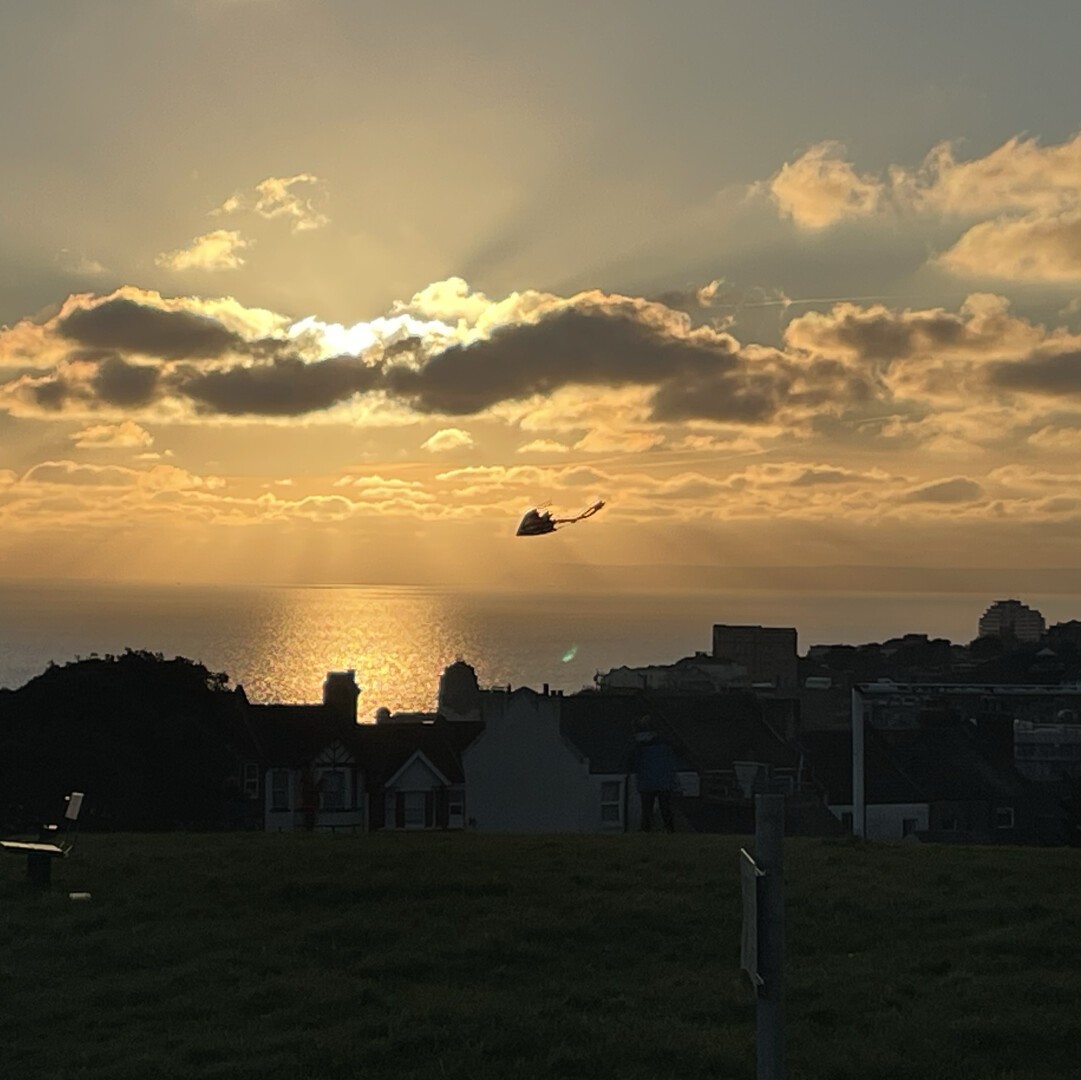 Sun behind clouds is setting over the sea while a silhouette of a kite is in the foreground