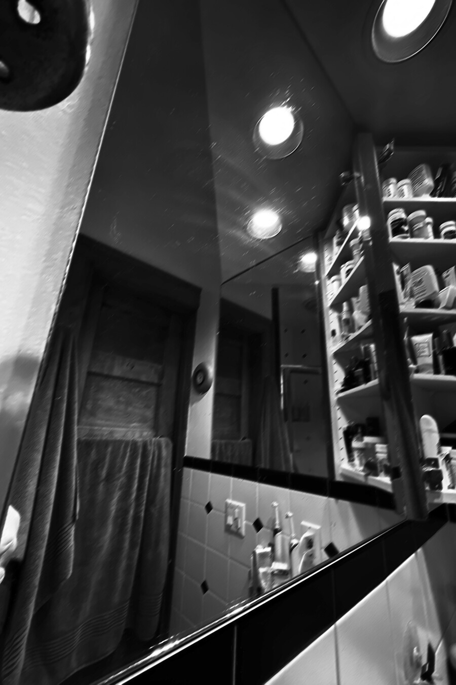 b&w, multiple mirrors in a small bathroom, with towels and shelves