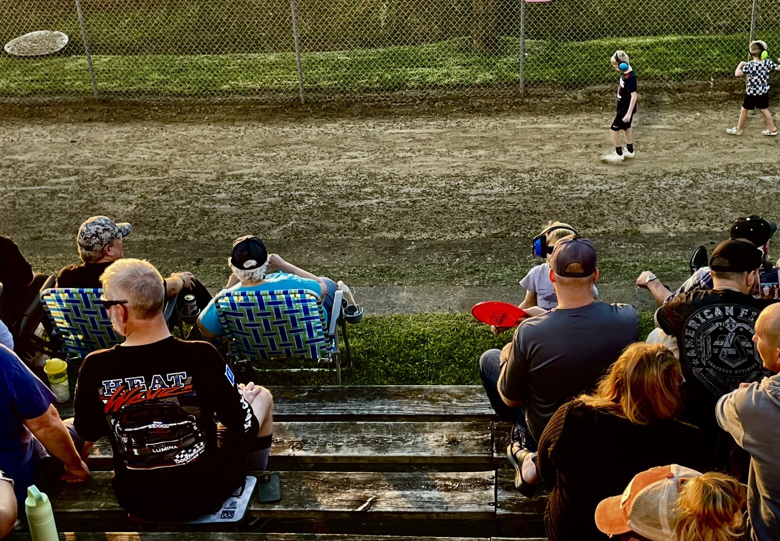 Many of the same people, still waiting. Two boys with ear protection are passing by.