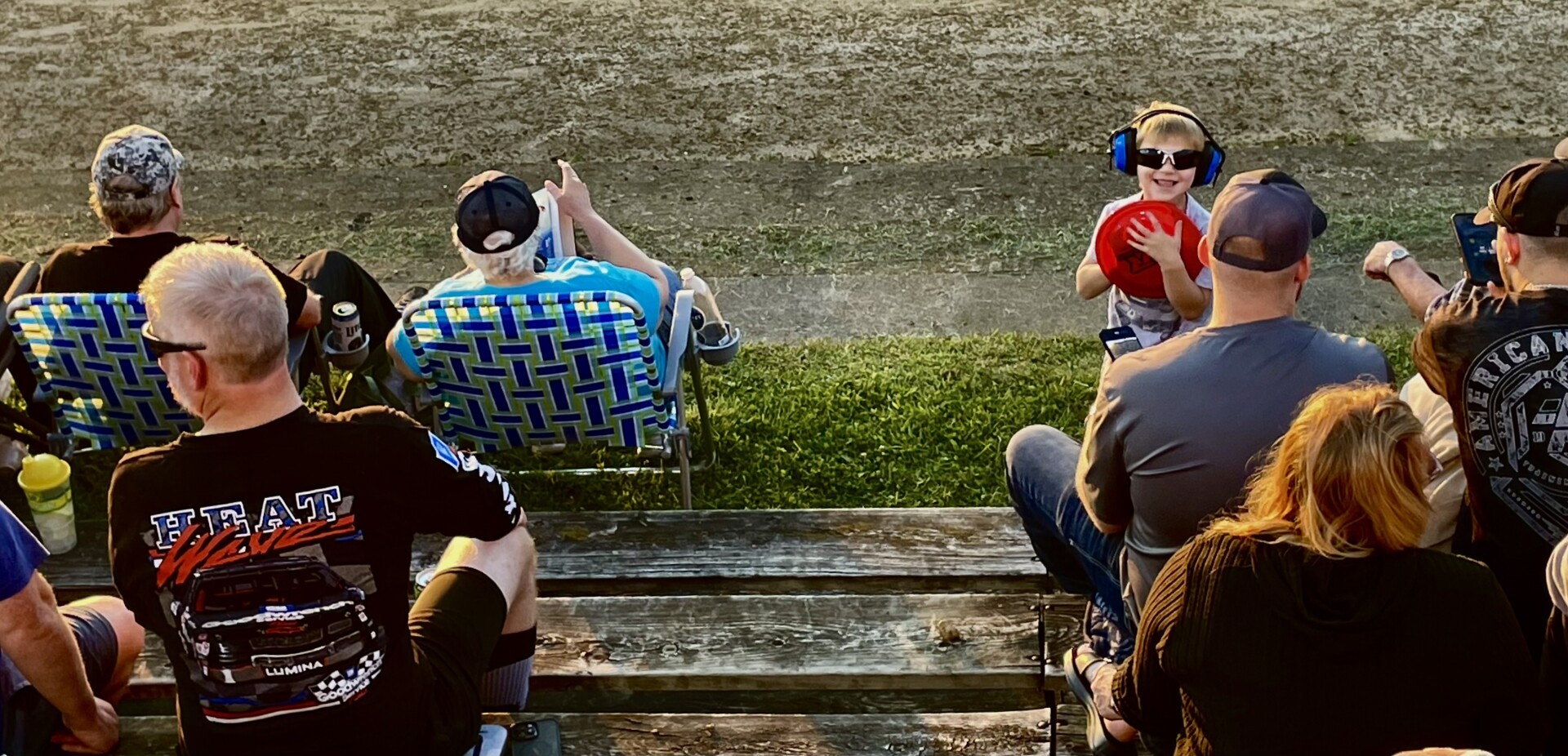 Adults still waiting. The first boy holds a frisbee. The sun is lower.