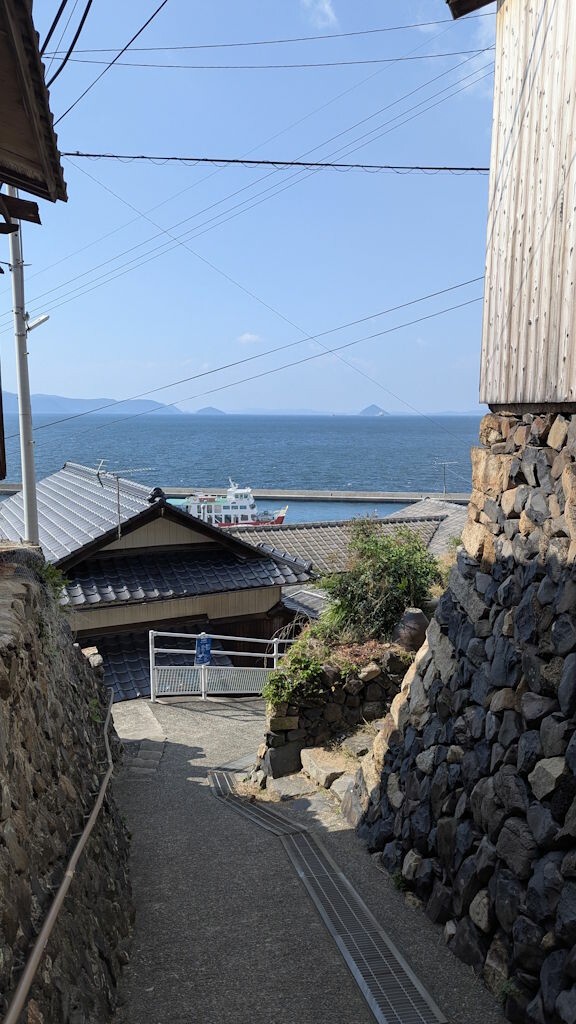 A street of Ogijima. It's narrow, goes downhill with a stunning view of the Seto Inland Sea in the background.
