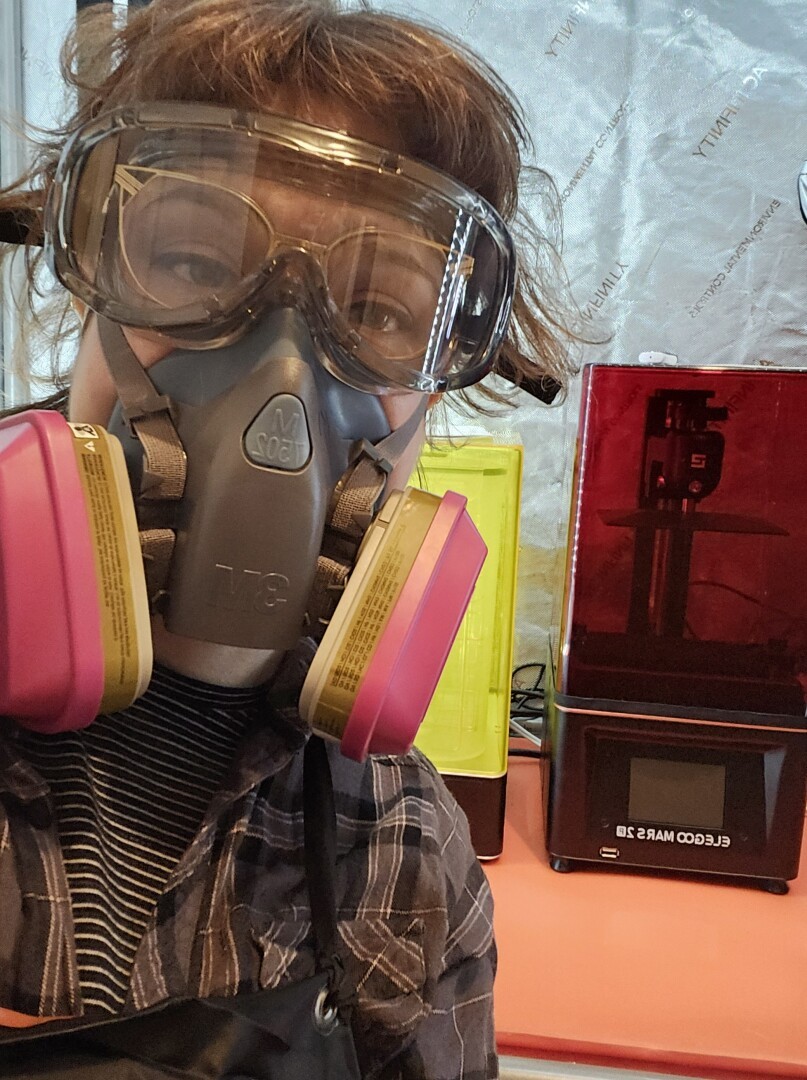 Oh hey, it's me in a pair of safety goggles and a heavy duty chemical mask. I'm standing in front if a 3D resin printer setup in a light and ventillation controlled tent. There are lots of clashing colors like neon yellow and dark red, orange and hot pink, and lo and behold there is a foil background. Wow. Such resin stench. Much facial smooshing. So many shinies and fan noises.