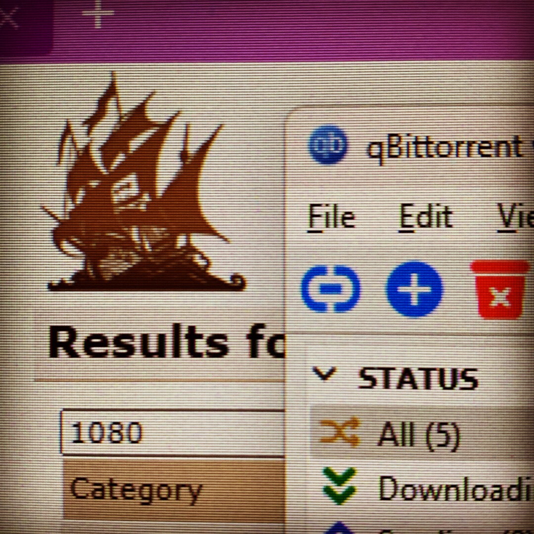 A screen off a desktop computer showing windows of qBittorrent and a website with a logo featuring a pirate ship