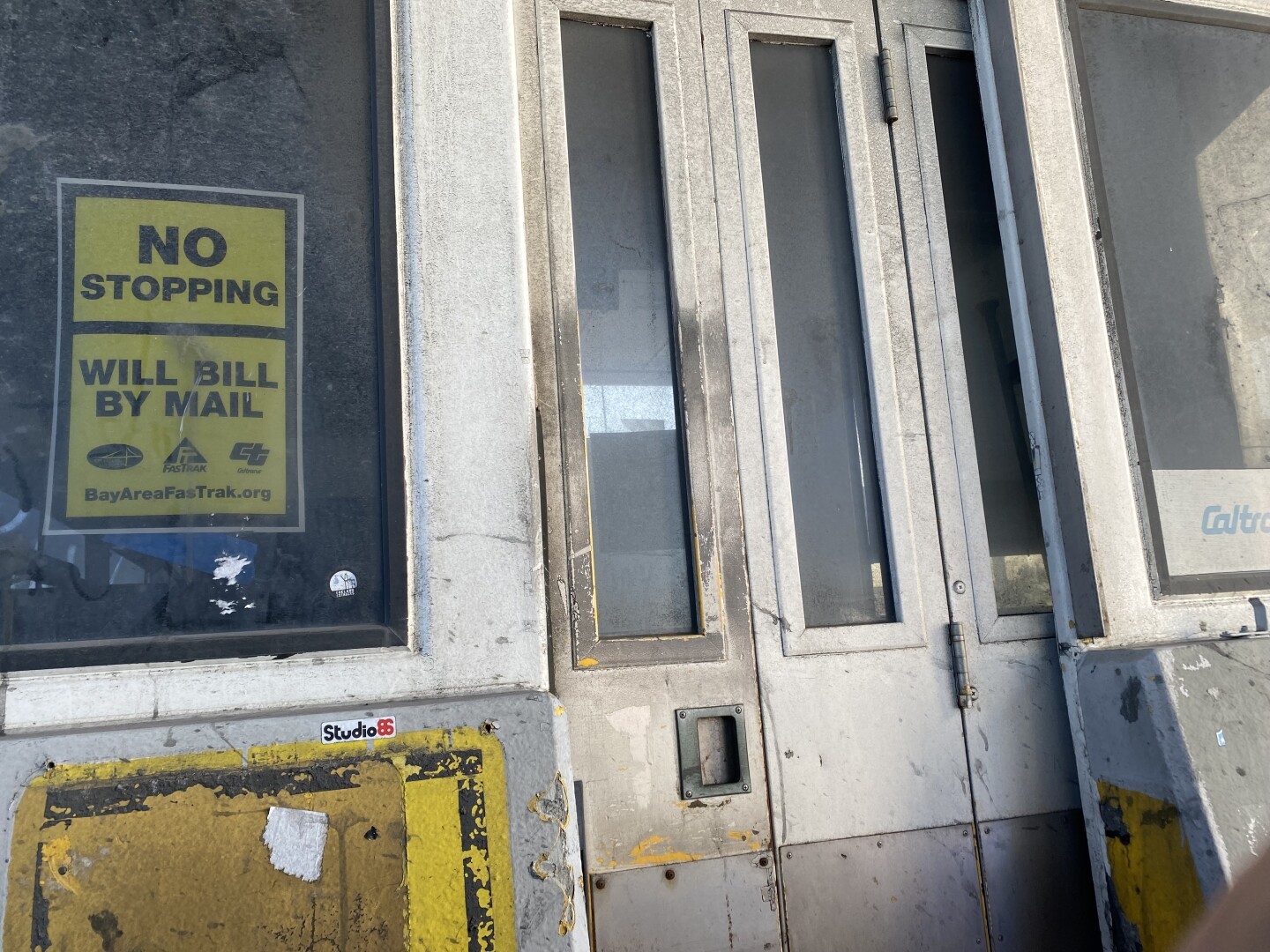 Long abandoned toll booth, dirty windows impossible to see through, dirty rusting metal doors, yellow sign: “No stopping Will bill by mail.”