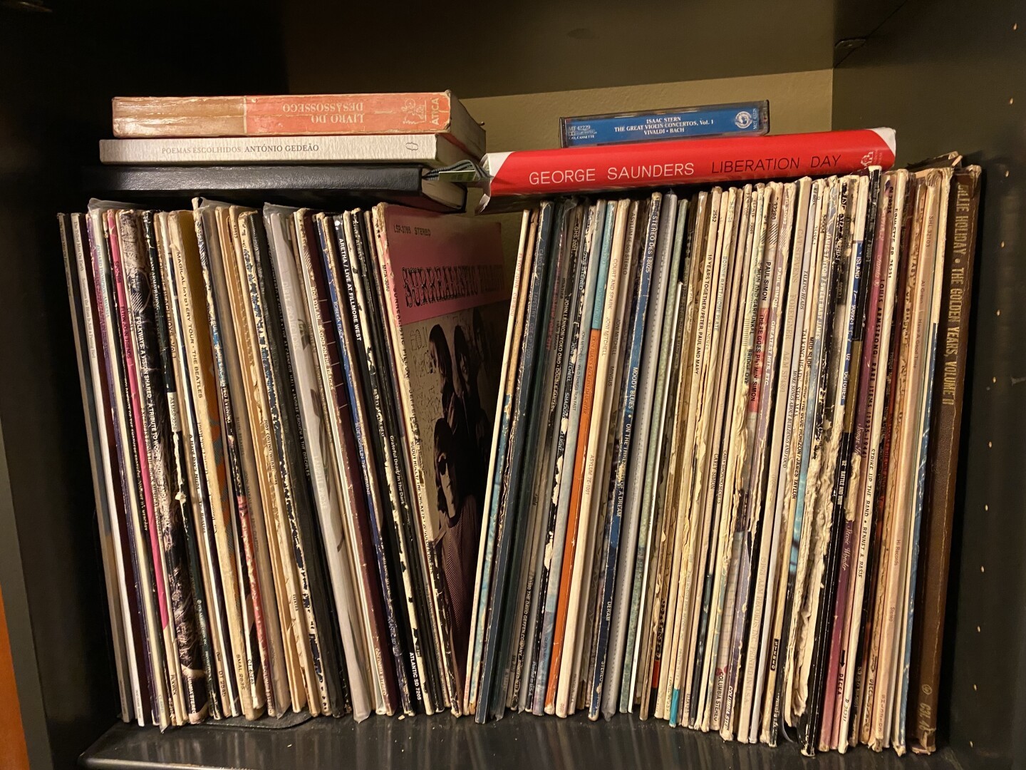 A shelf of old records with books and a cassette tape laying on top.