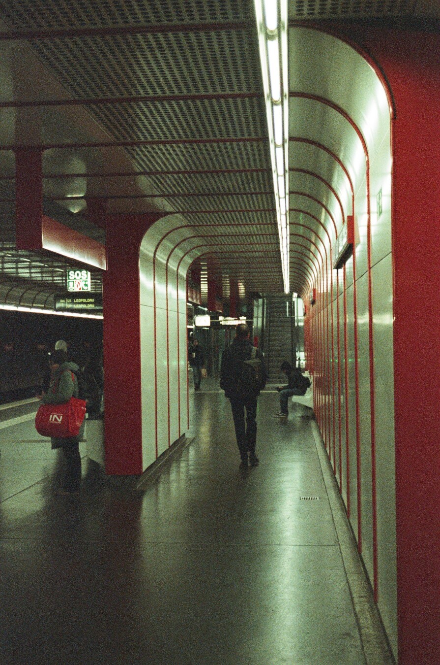 A photograph of a underground metro station with white and red panels, pople hanging around