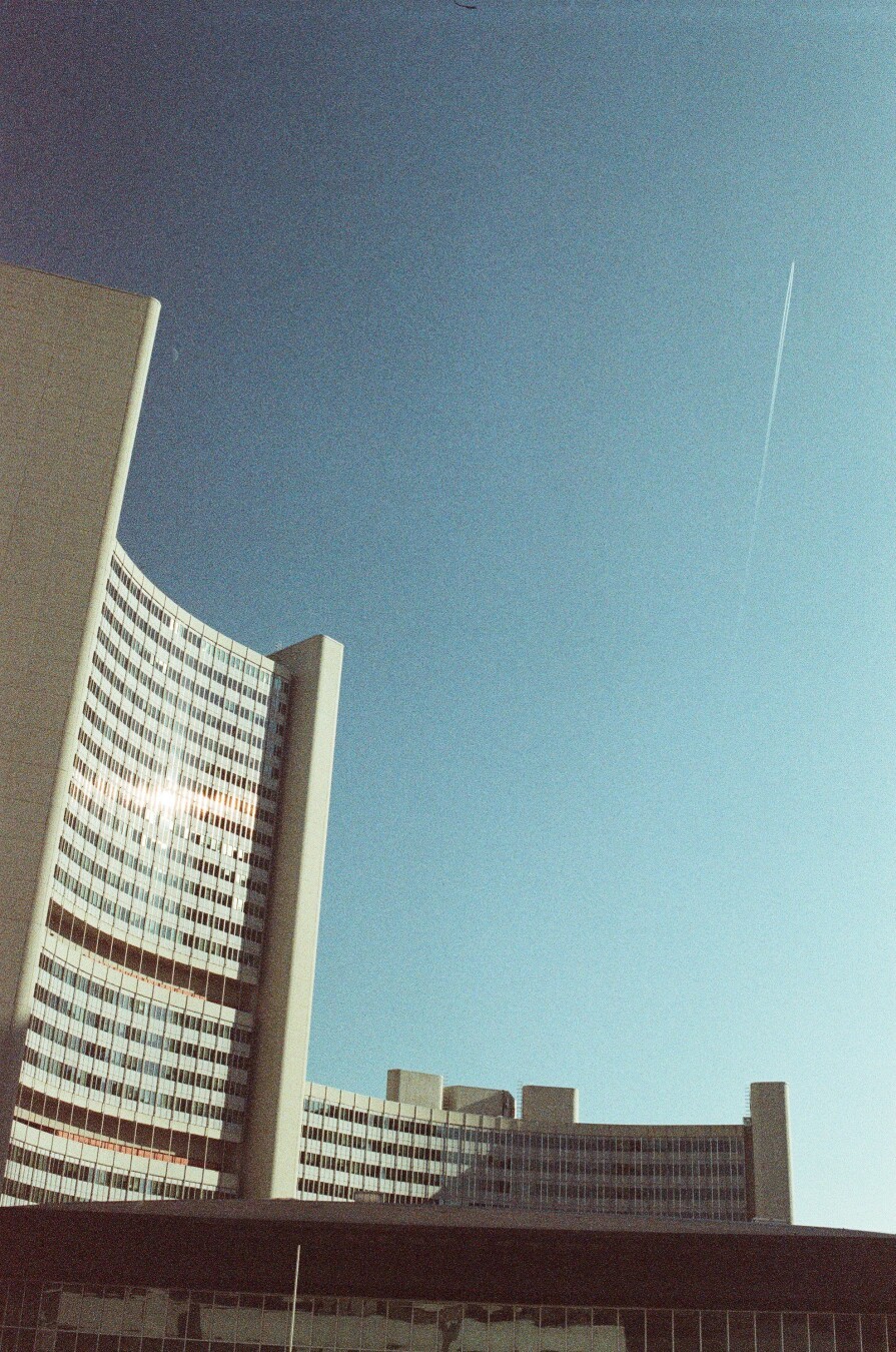 A photo of an arching monumental building on the side, blue sky and a plane trail on the right.