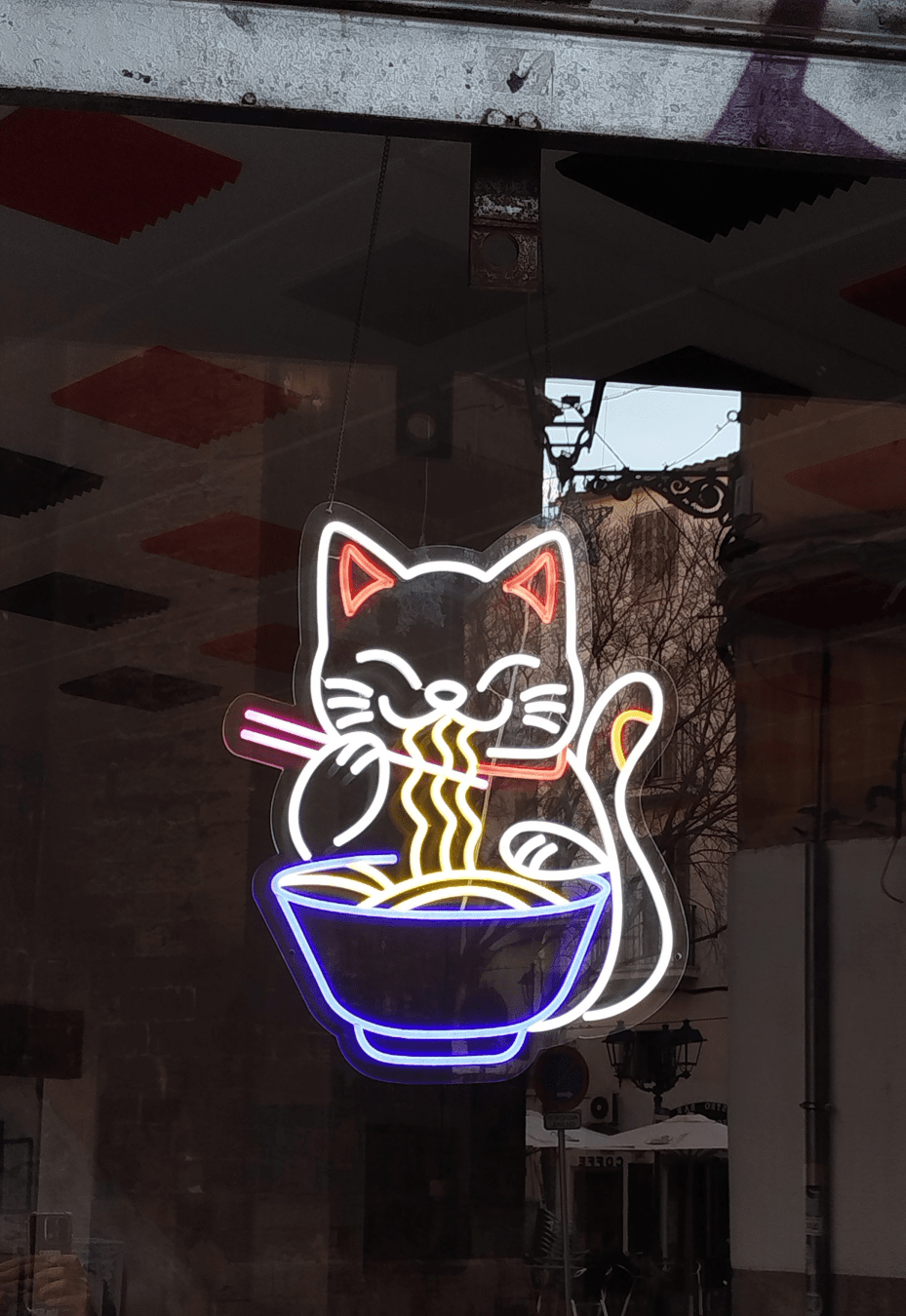 Escaparate con lámpara de neón con forma de gato comiendo ramen.