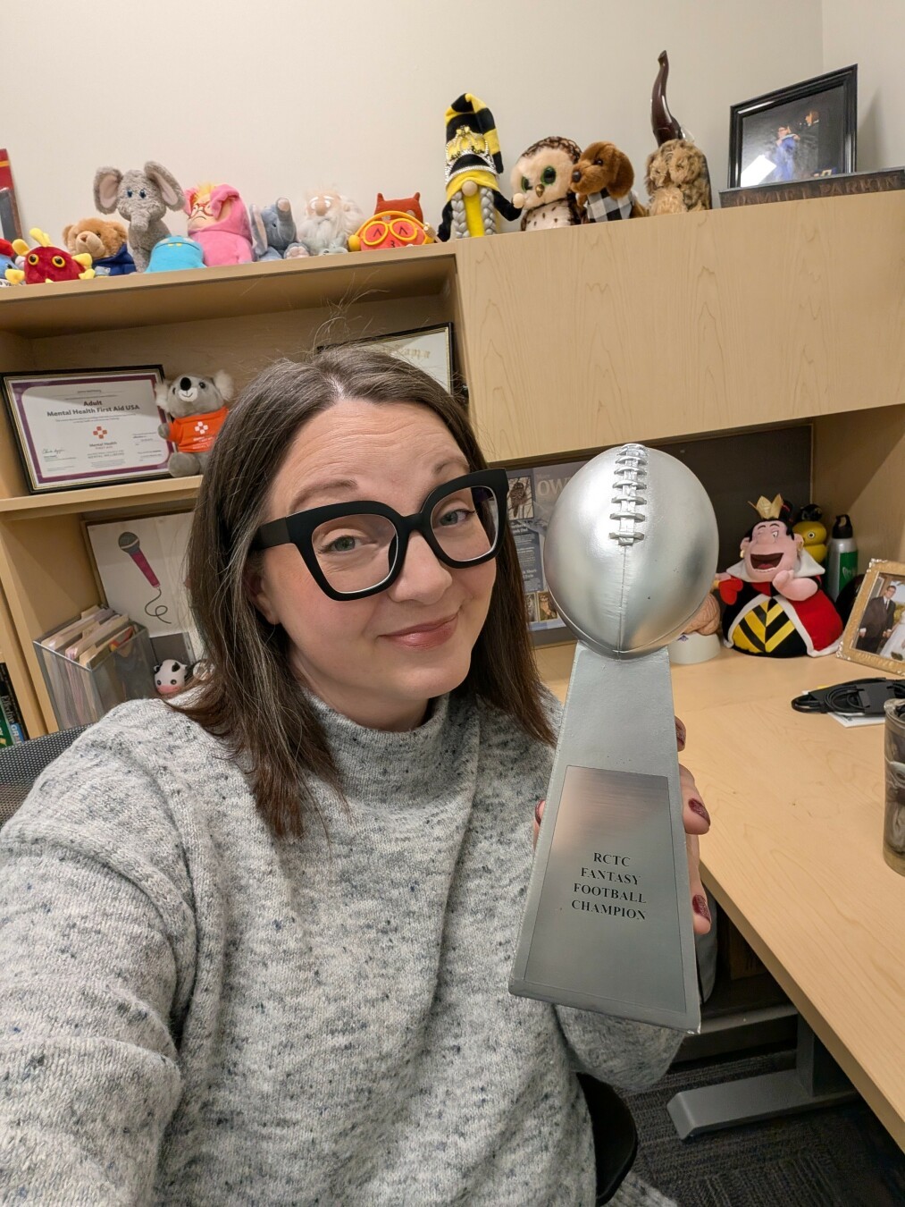 A woman looking proudly at the camera holding a silver trophy topped with an American football.