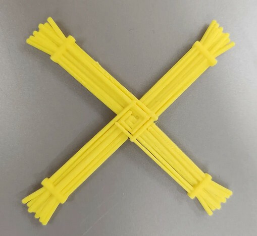 A yellow painted 3D print of Brigids Cross on a gray table.