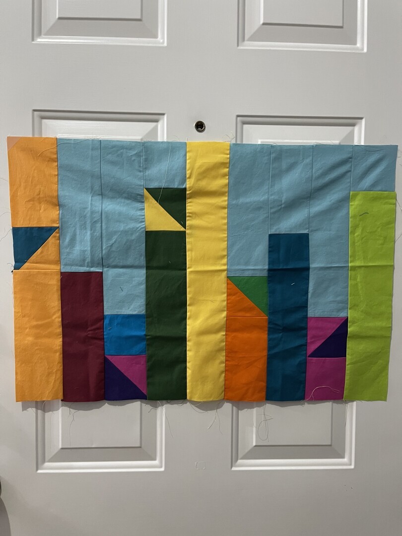 A block for the murder mystery quilt 2025. Includes shades of yellow, blues, reds/pinks, oranges, and greens. Pieced together with half square triangles, and 3.5in strips inspired by the Incan form of record keeping called quipus.