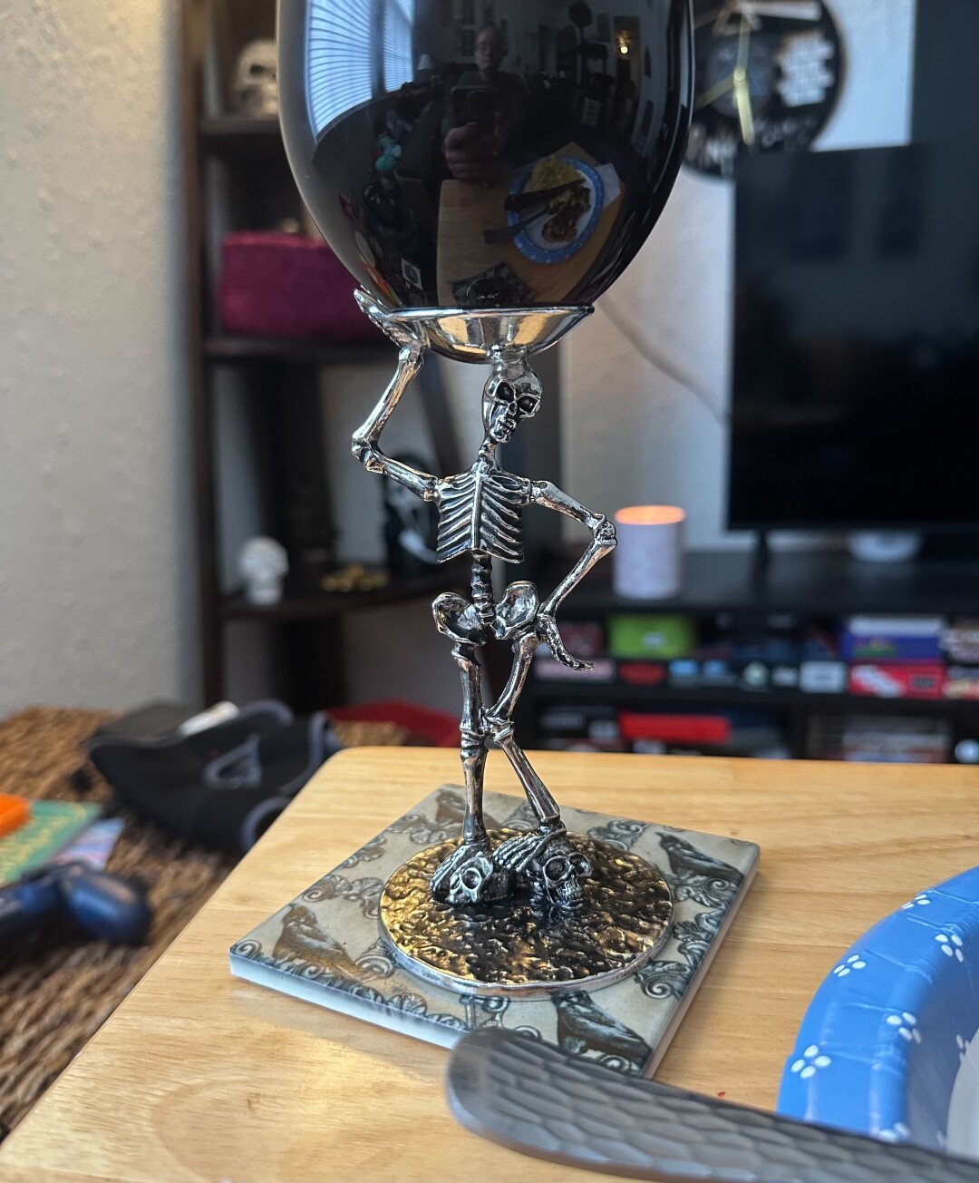 A wine glass with a pewter skeleton as a stem sits on a ceramic coaster.