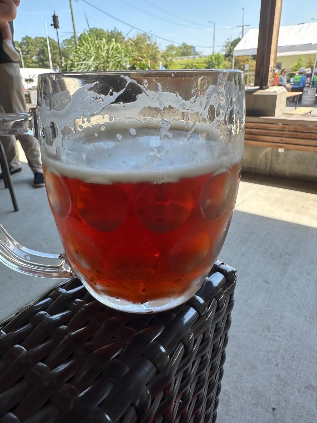A glass filled with beer sits on a rattan armrest on a brewery patio