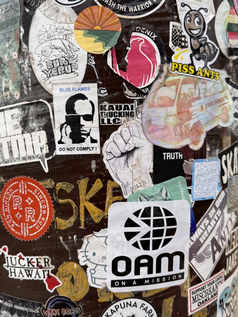 Various stickers covering a light pole and its attached electrical box.