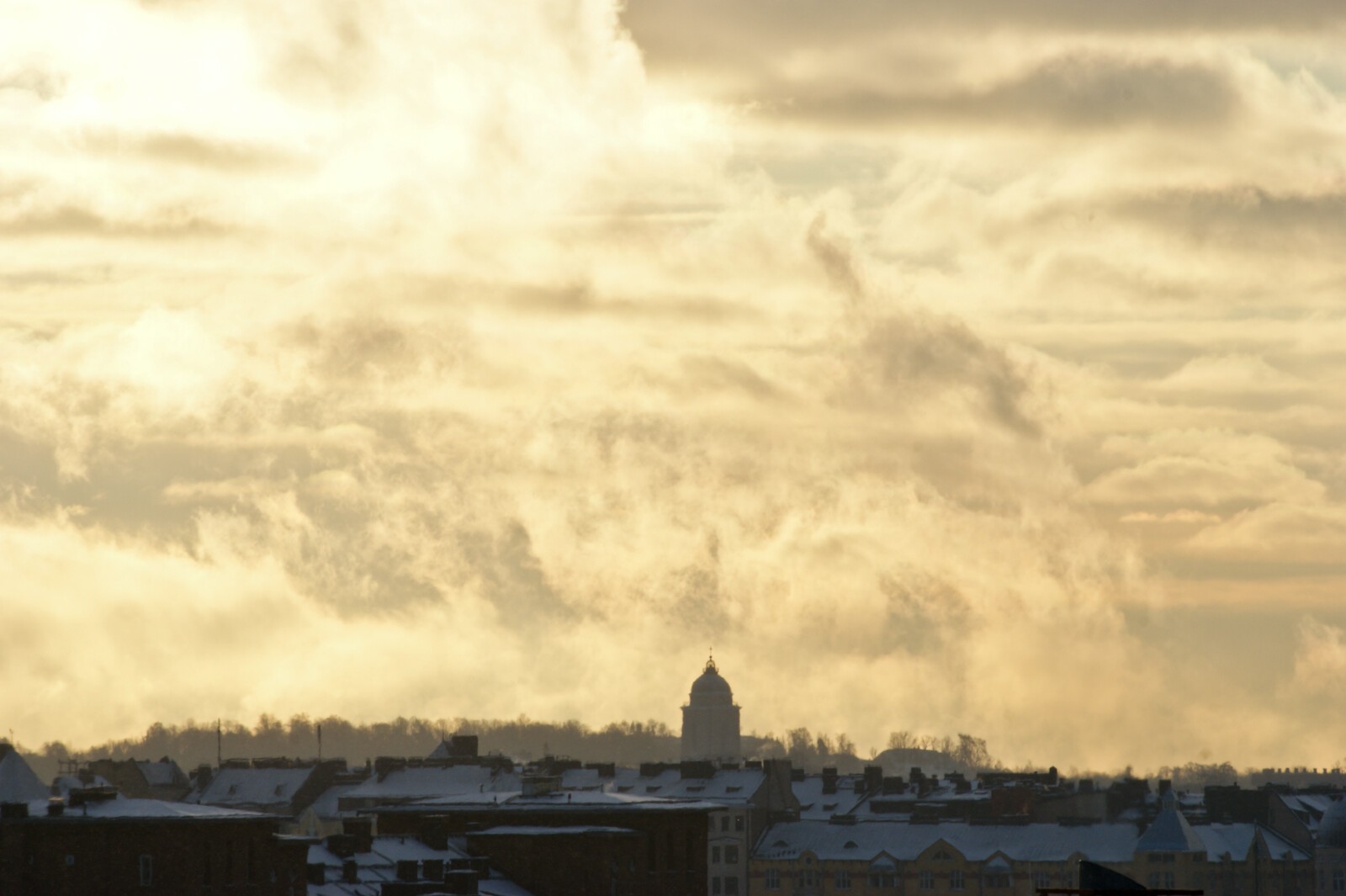 Foreground roofs of a city, background clouds in sunrise light.
