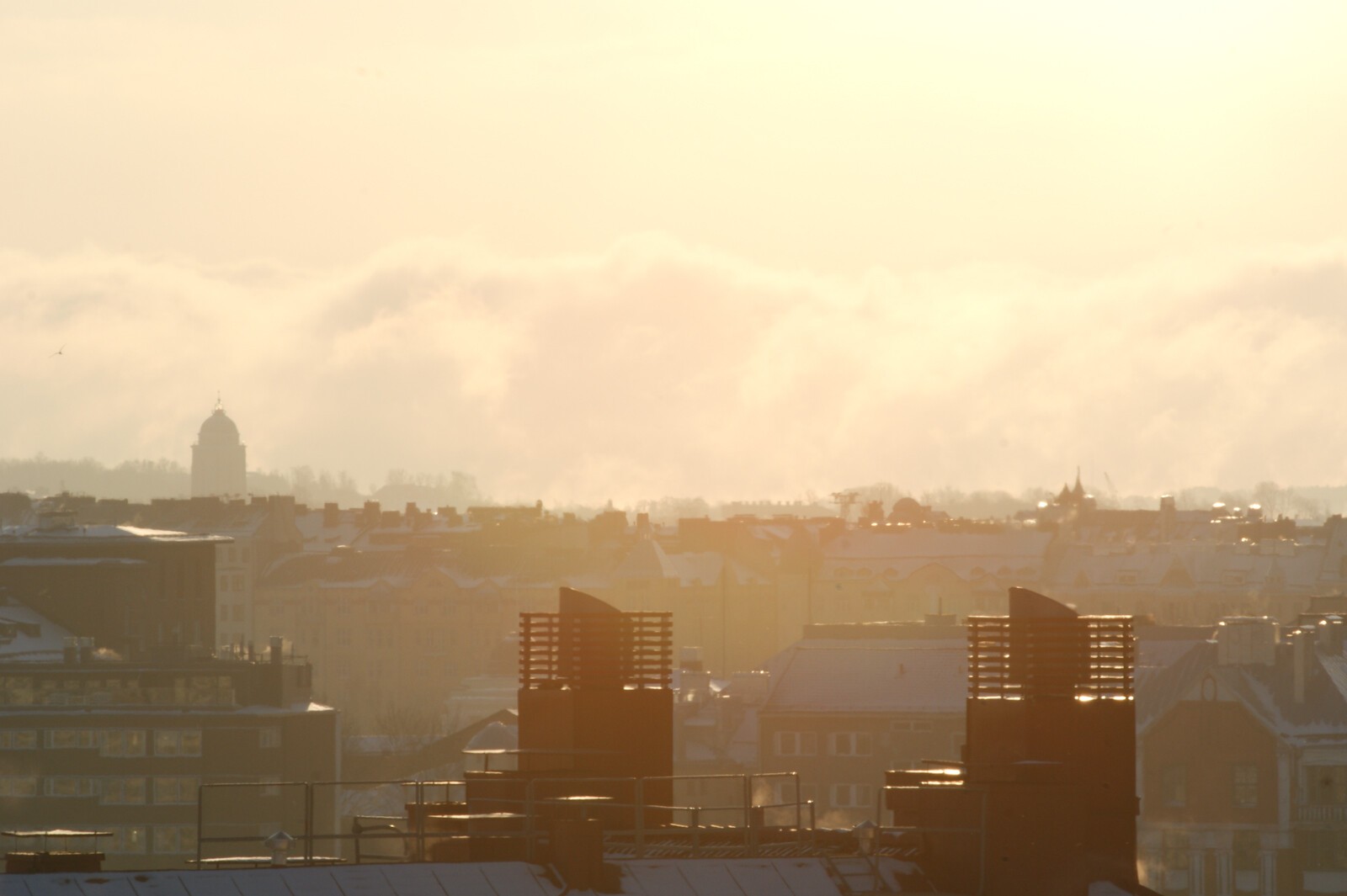 Foreground roofs of a city, background clouds in sunrise light.