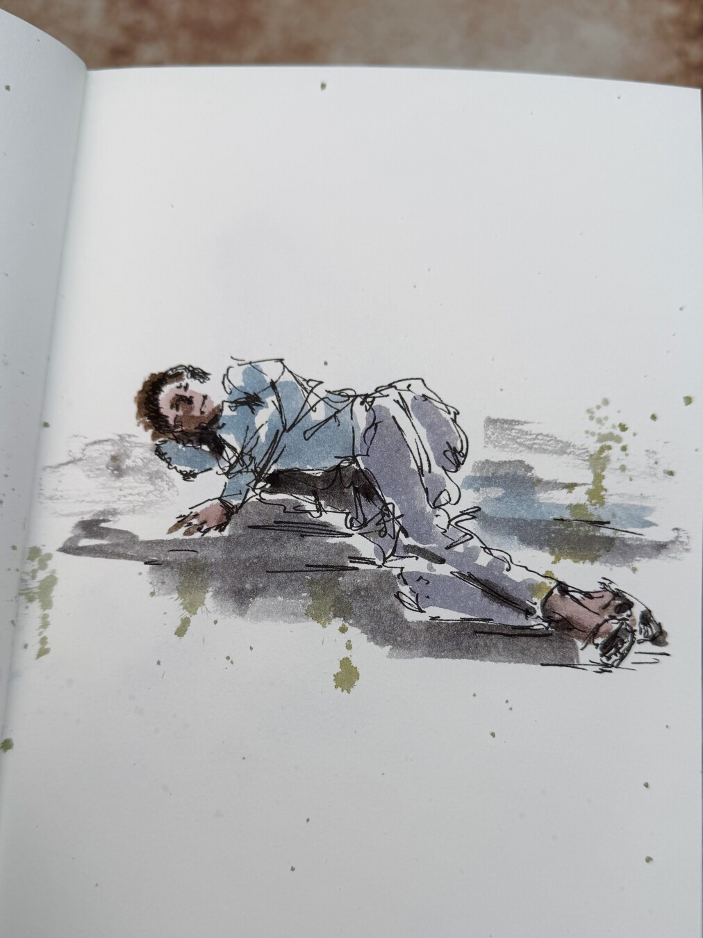 A pose of someone lying on her side on the ground with right arm under the head and left arm to the front. Feet crossed, to the foreground. Scribbled black ink lines filled in with watercolour. Brown hair blue shirt and purple grey trousers and wa wearing sandals.