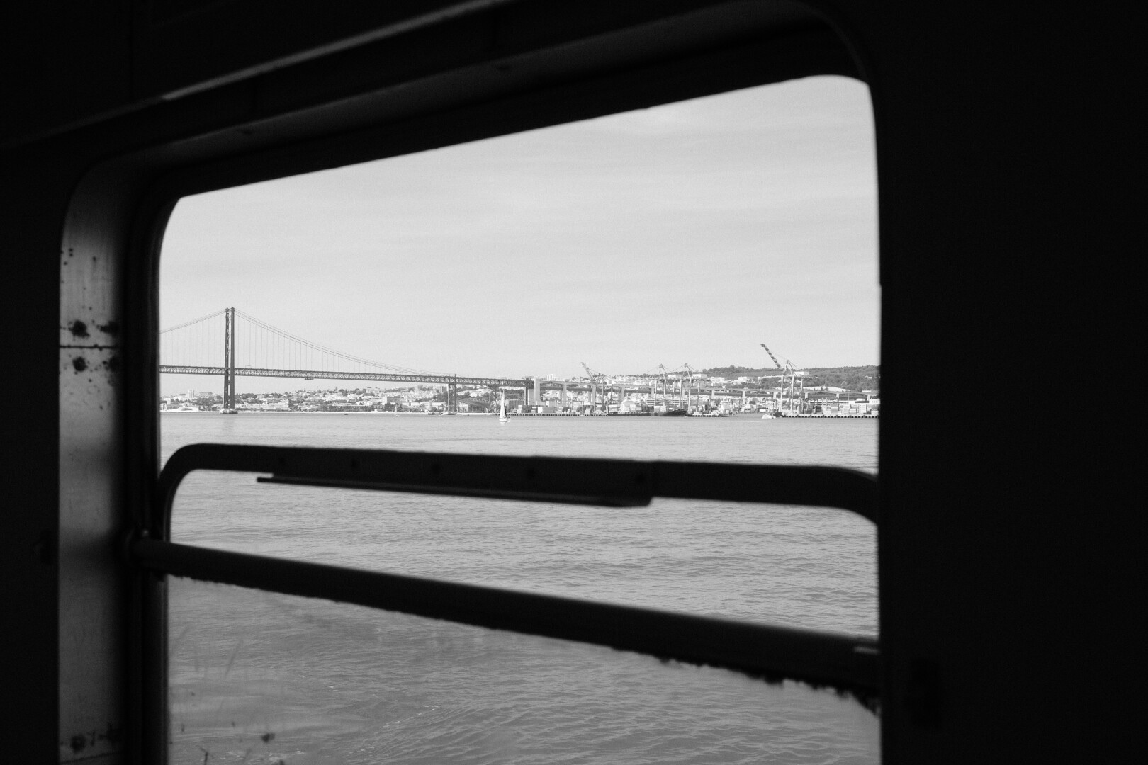 Be picture of a ferry window, while crossing the Tagus River. In the background is the 25 de Abril bridge