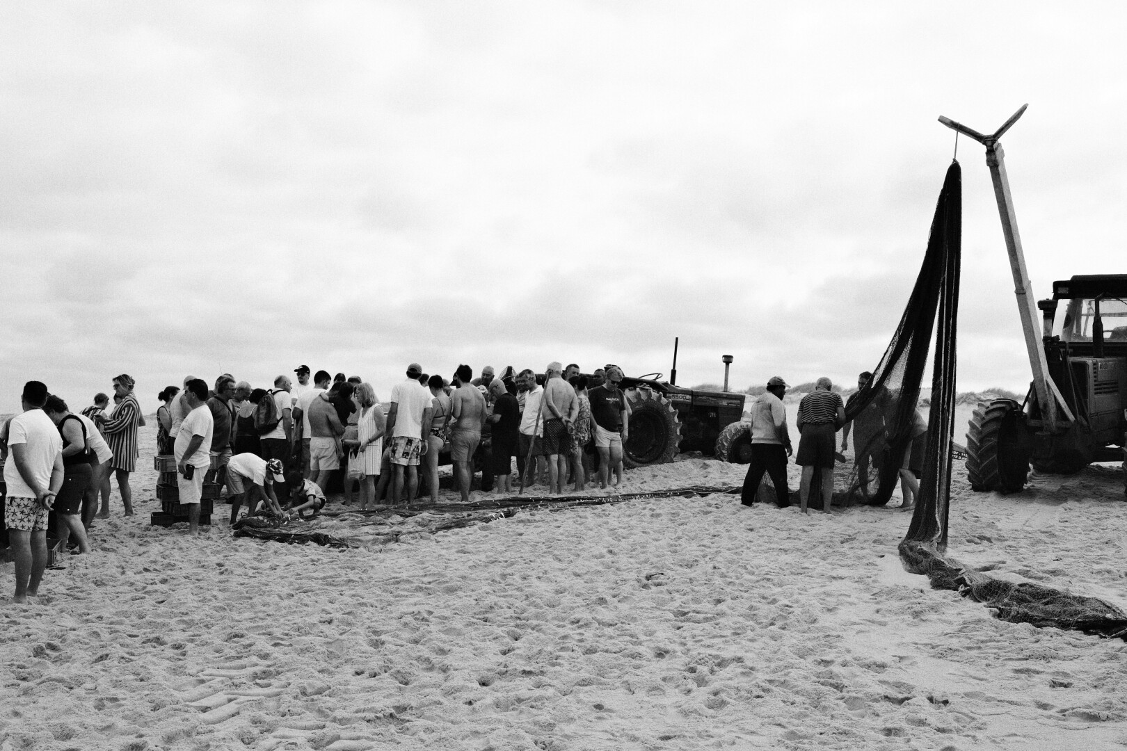 BW picture of the fishing net, hanging from a metal arm, that is attached to the tractor. On the left side a significant crowd.