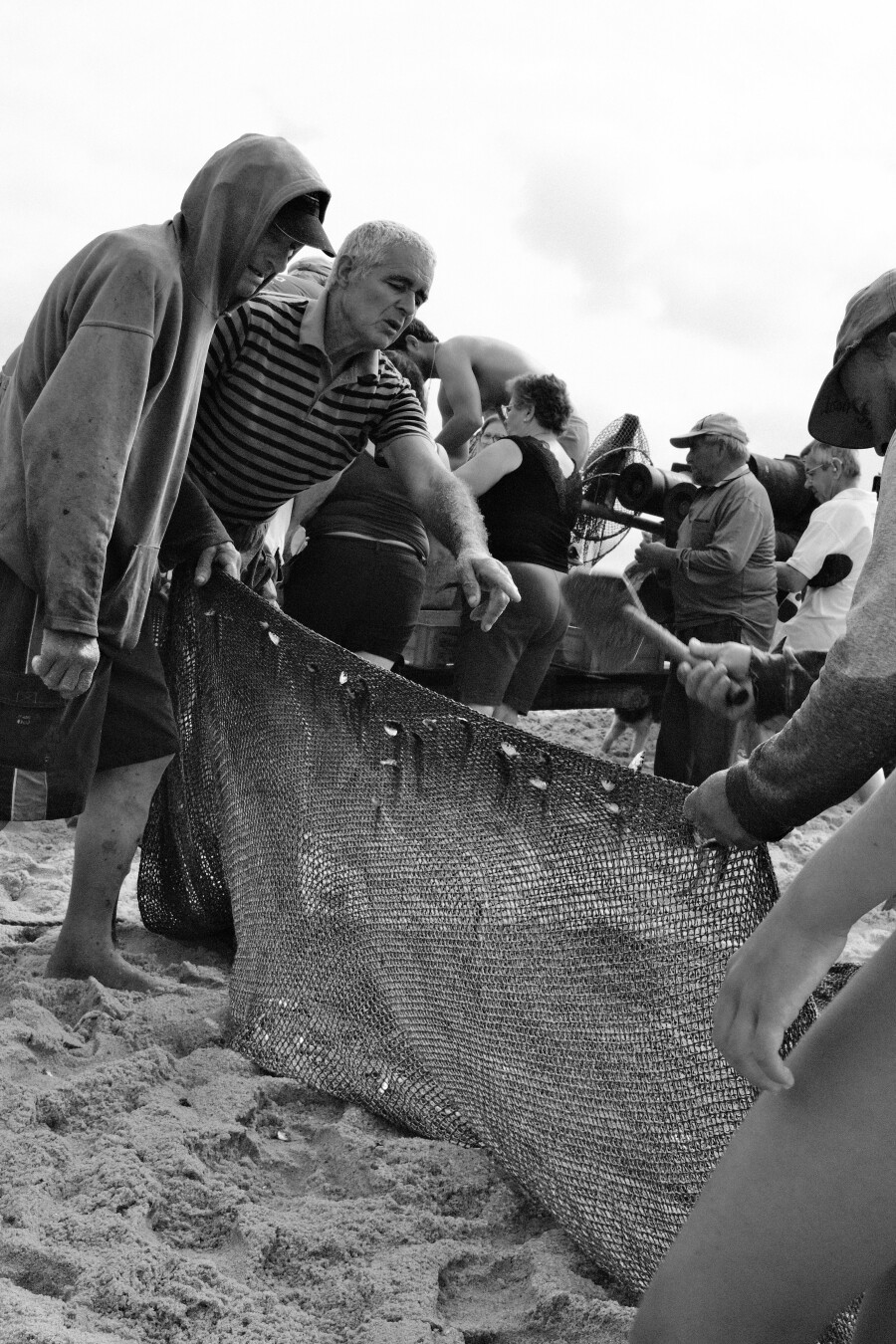 BW picture of a couple fishermen cleaning up a net. One of them is pointing with his arm and shouting some instructions.