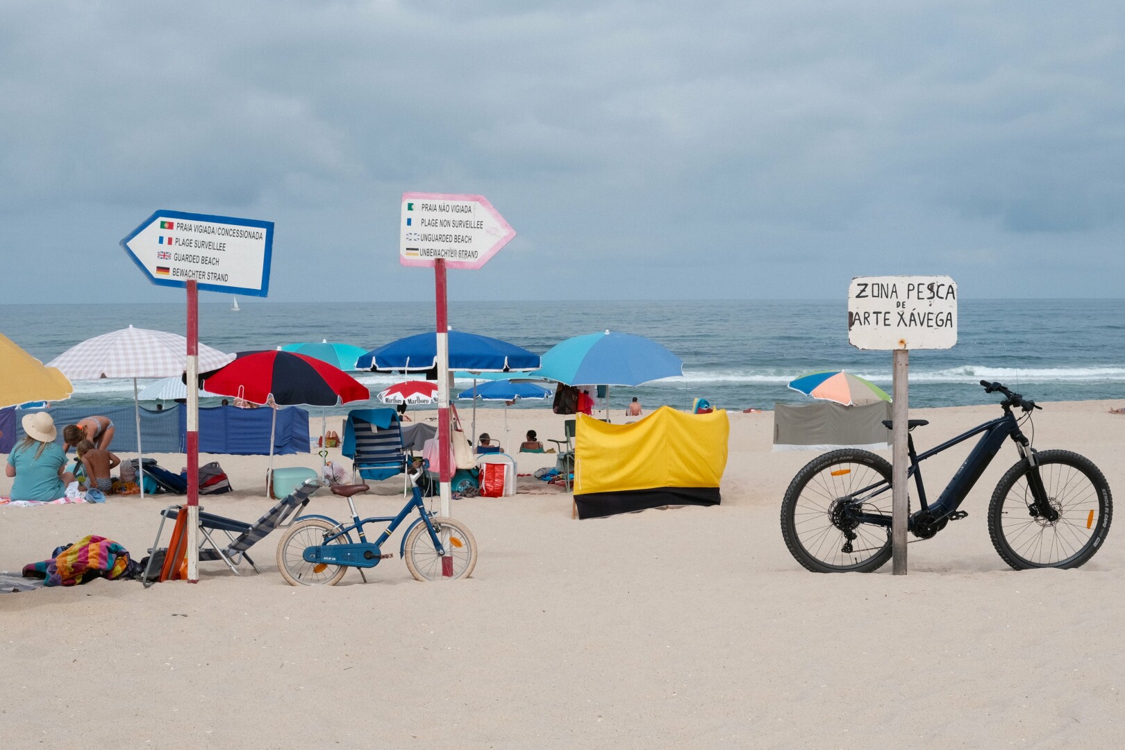 Picture of Praia da Tocha. Three signs are identifying the guarded (to the left) and the unguarded beach (to the right), as well as the fishing area. Two bicycles, one from an adult and one from a child are leaning against the signs.