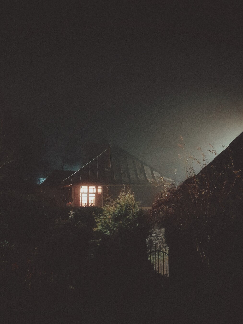 A window lit up early in the morning on a foggy, rainy day.