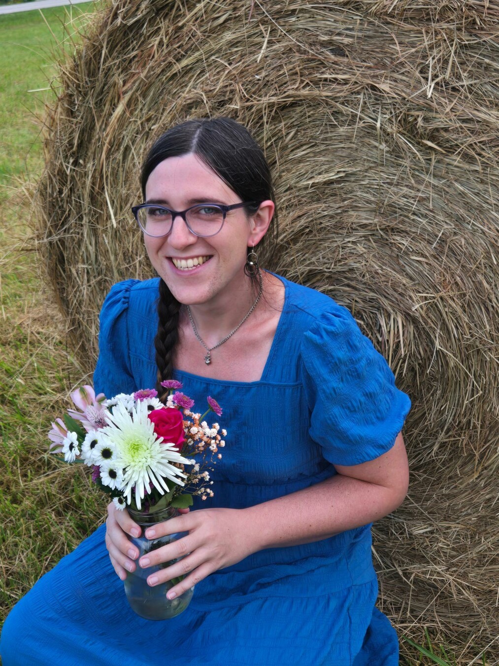 Close up shot of white trans woman in front of hay bale with flowers.