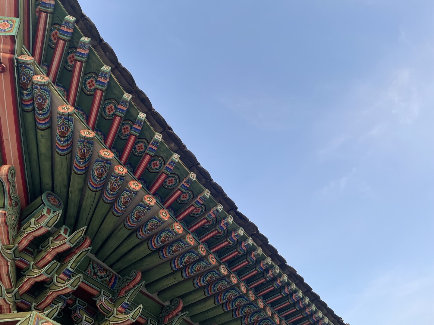 Half of the picture shows the intricately painted green and red underside of the roof of the entrance gate to the palace ground. The other half shows a blue sky.