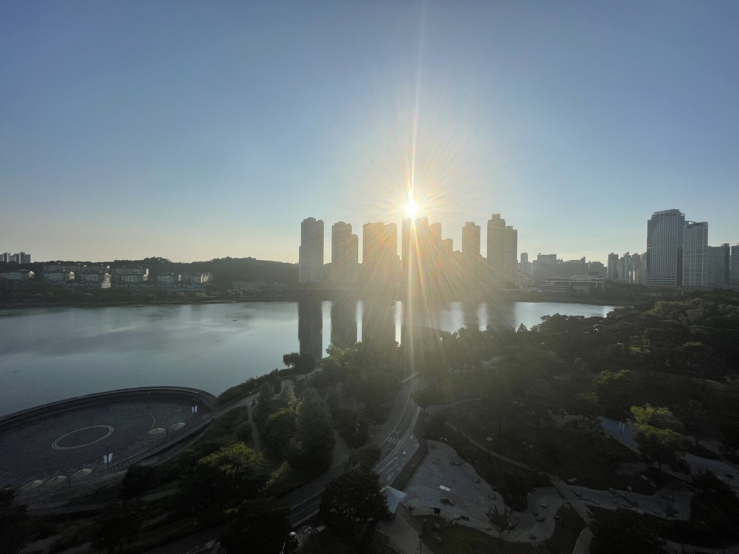 The sun starting to set over a group of high rises on the opposite side of the lake.