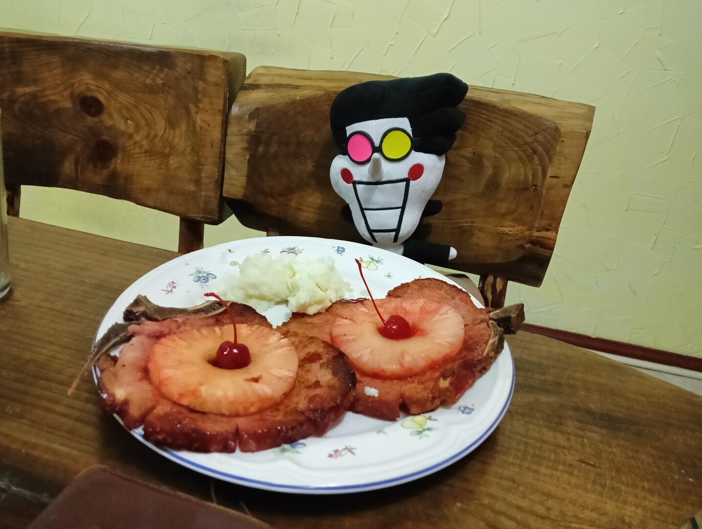 Photo of a Christmas dinner from a few years ago, on a wooden table there is a plate with pork chops with large slices of pineapple and a cherry in the center, and mashed potatoes.