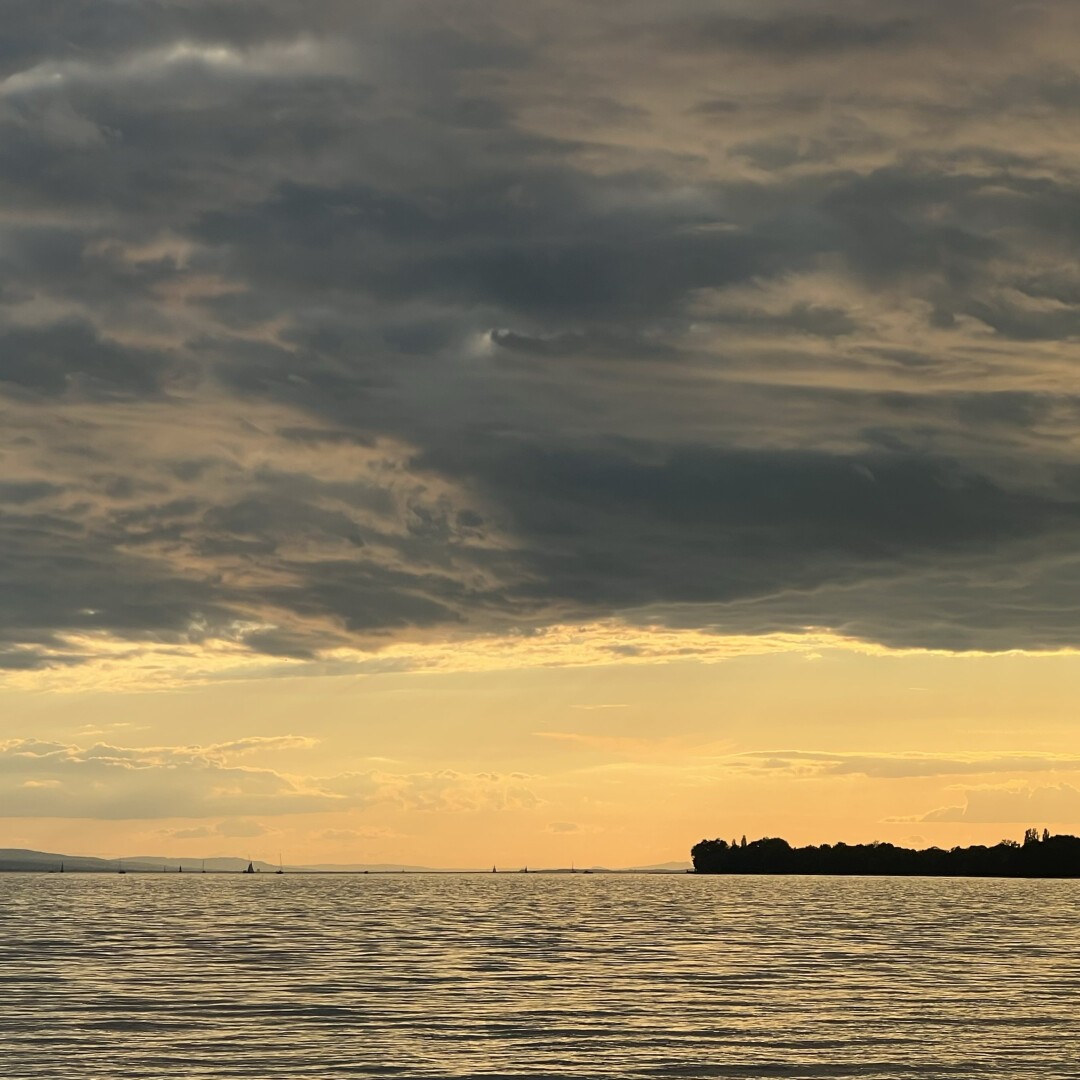 A golden sunset over a lake that stretches to the horizon. Above are clouds, illuminated from below by the reflections of the sun in the water.