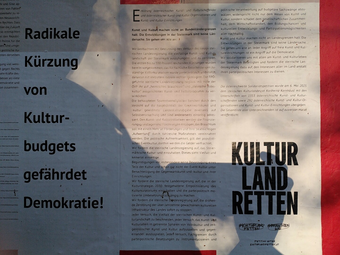 A wallpaper shows an article about cuts in cultural funding. The shadow of the photographer holding a smartphone covers a third of the image.
