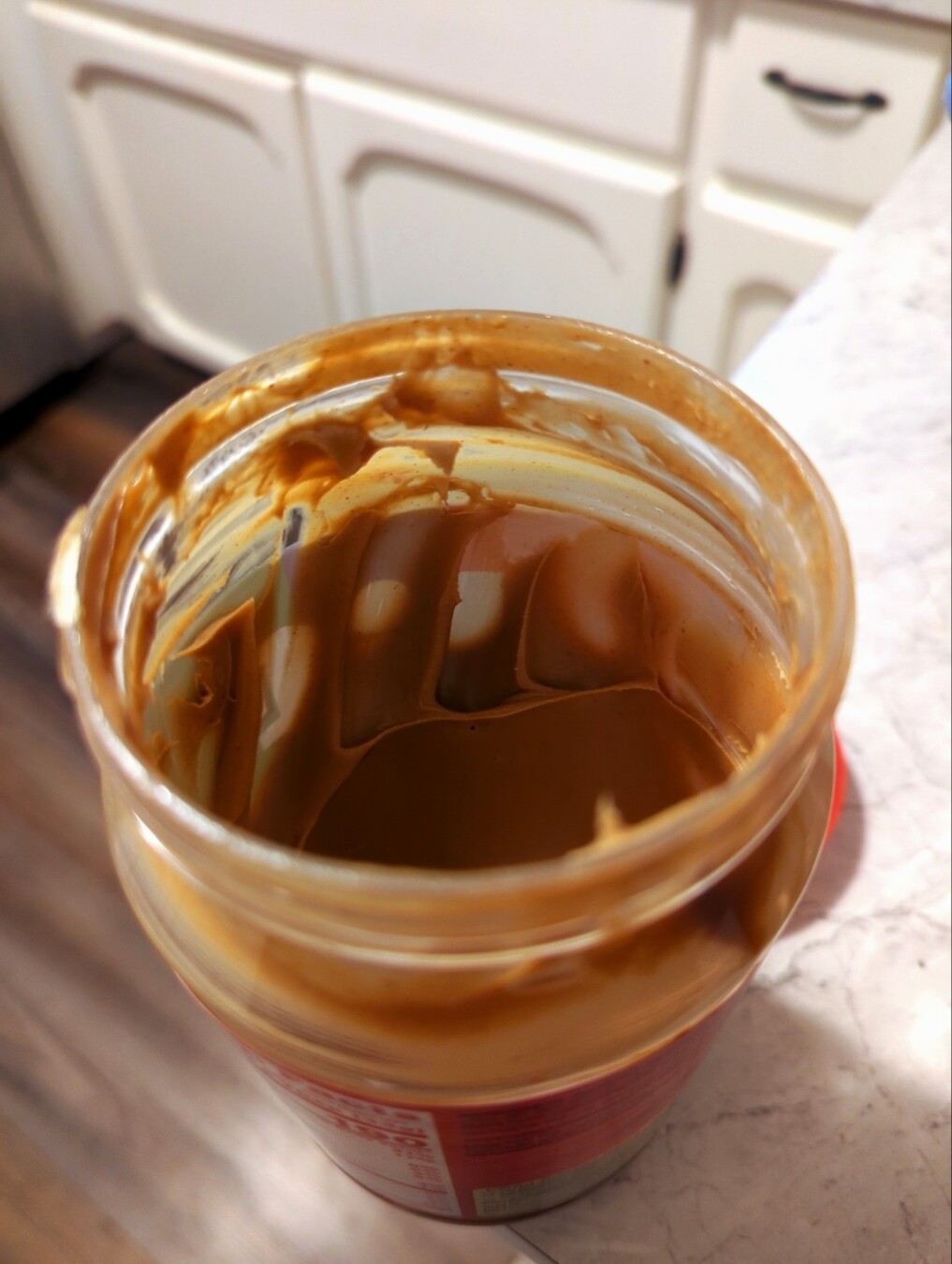 An opened container of peanut butter that clearly shows where 4 fingers scooped out a large amount of peanut butter.