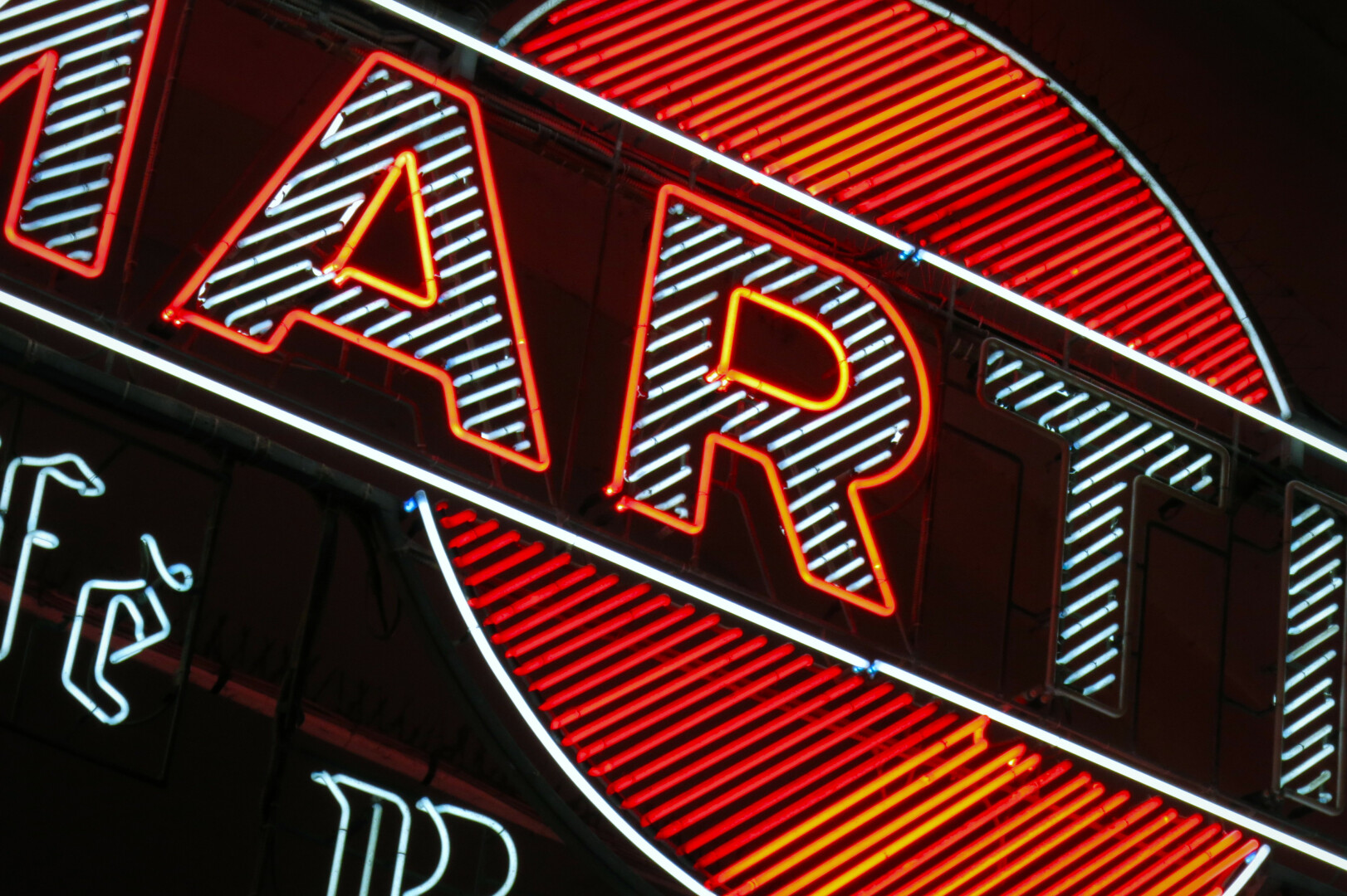 Ausschnitt einer leuchtenden Neonwerbung bei Nacht. Sie zeigt das Logo der Marke "Martini". Der Schriftzug ist aber nur zum Teil zu sehen.